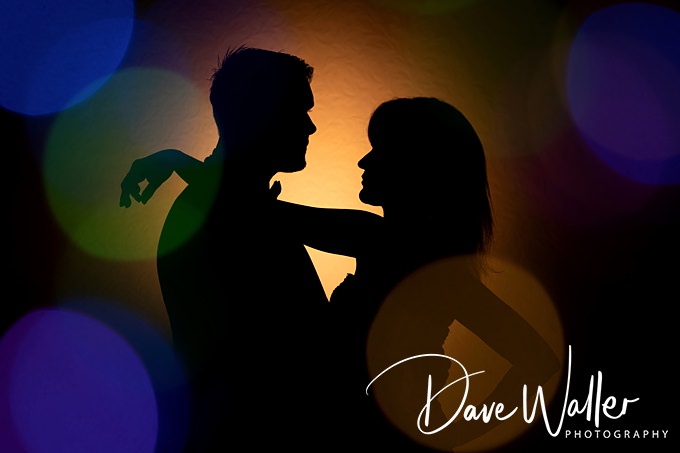 Silhouettes of a couple dancing against a warm, glowing background with colorful bokeh lights evoke a romantic, intimate atmosphere. Perfect for a wedding moment captured by any talented photographer in Lincoln.