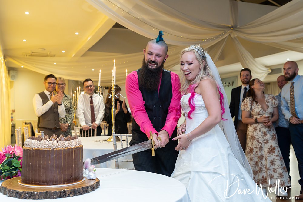 Bride and groom cutting cake with guests watching.