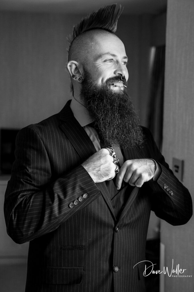 Bearded man in suit with piercings smiling confidently.
