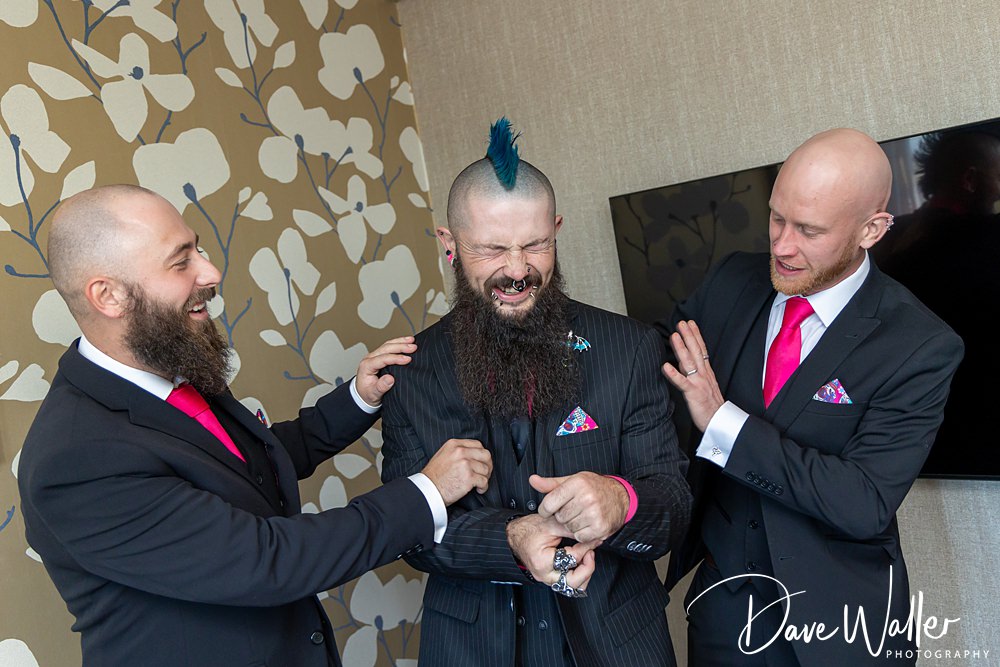 Three men laughing in colourful suits indoors.