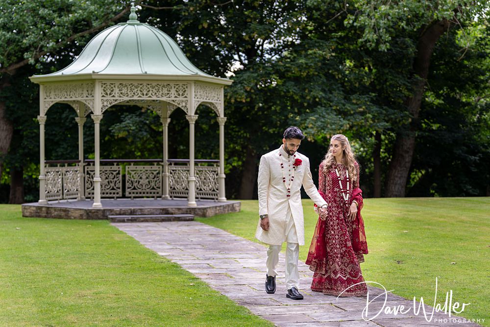 Couple walking near ornate park gazebo in traditional attire.