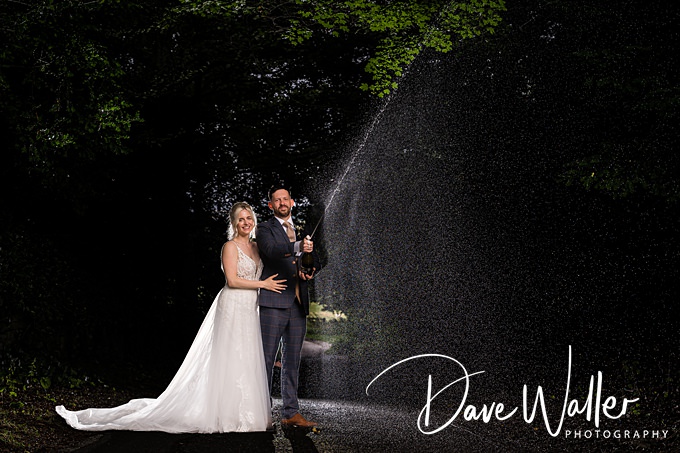 Couple celebrating with champagne spray in forest.