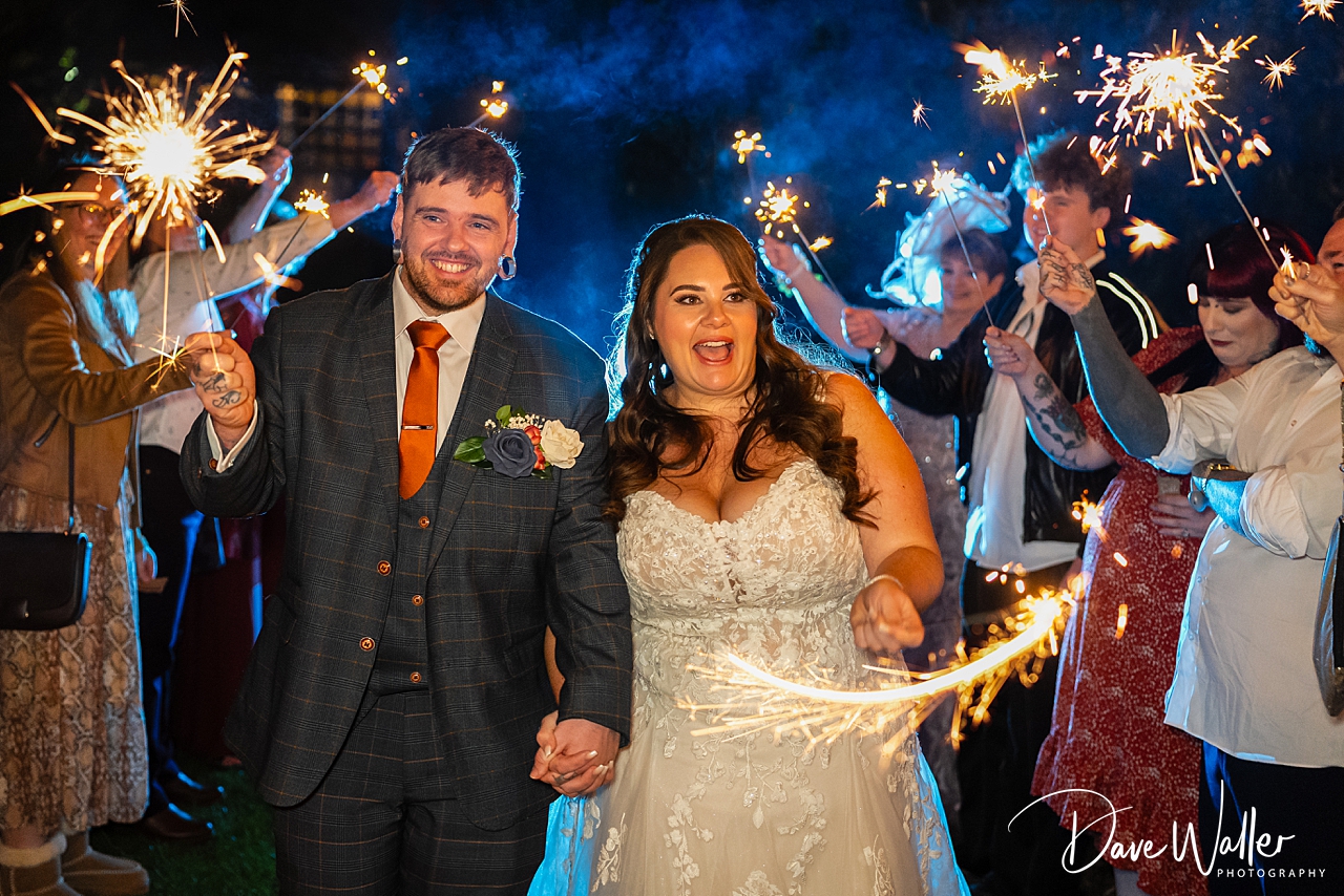 Happy couple surrounded by sparklers during wedding celebration.