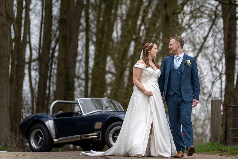 Smiling bride and groom walking by vintage car.