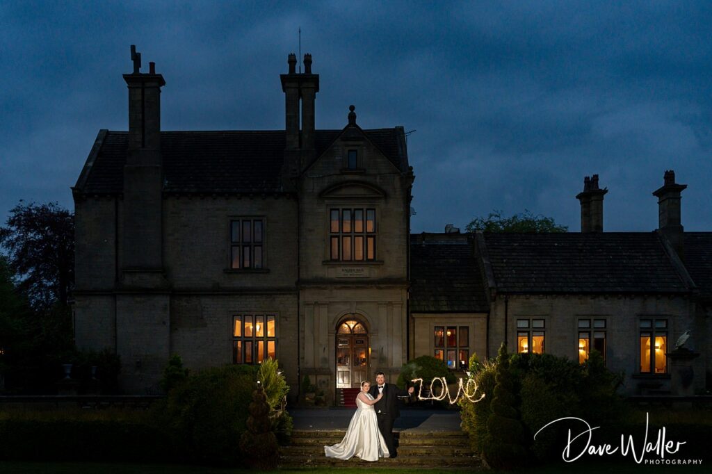 Bride and groom outside illuminated manor at night