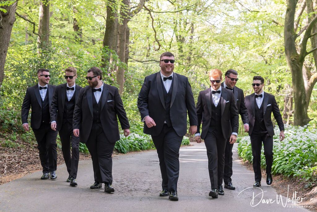 Groomsmen in black tuxedos walking through woodland path