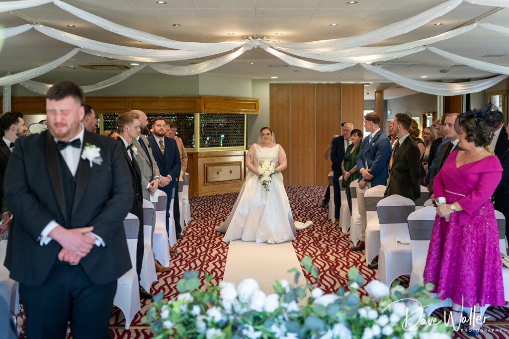 Bride walking down aisle at indoor wedding ceremony