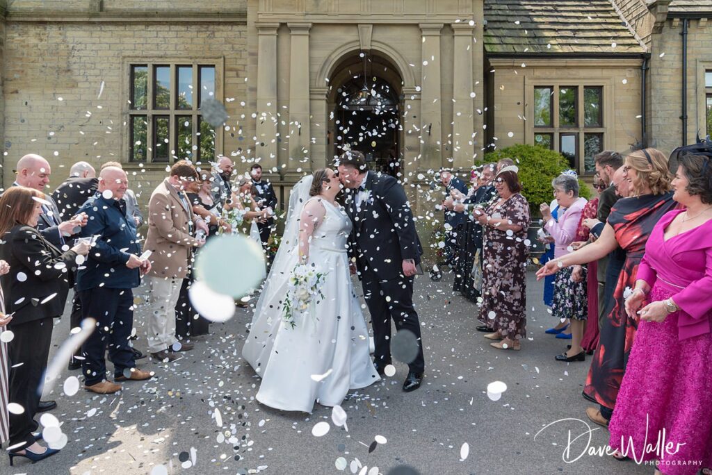 Bride and groom kissing amid confetti outside venue