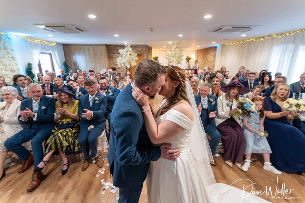 Bride and groom kissing, guests applauding at wedding.
