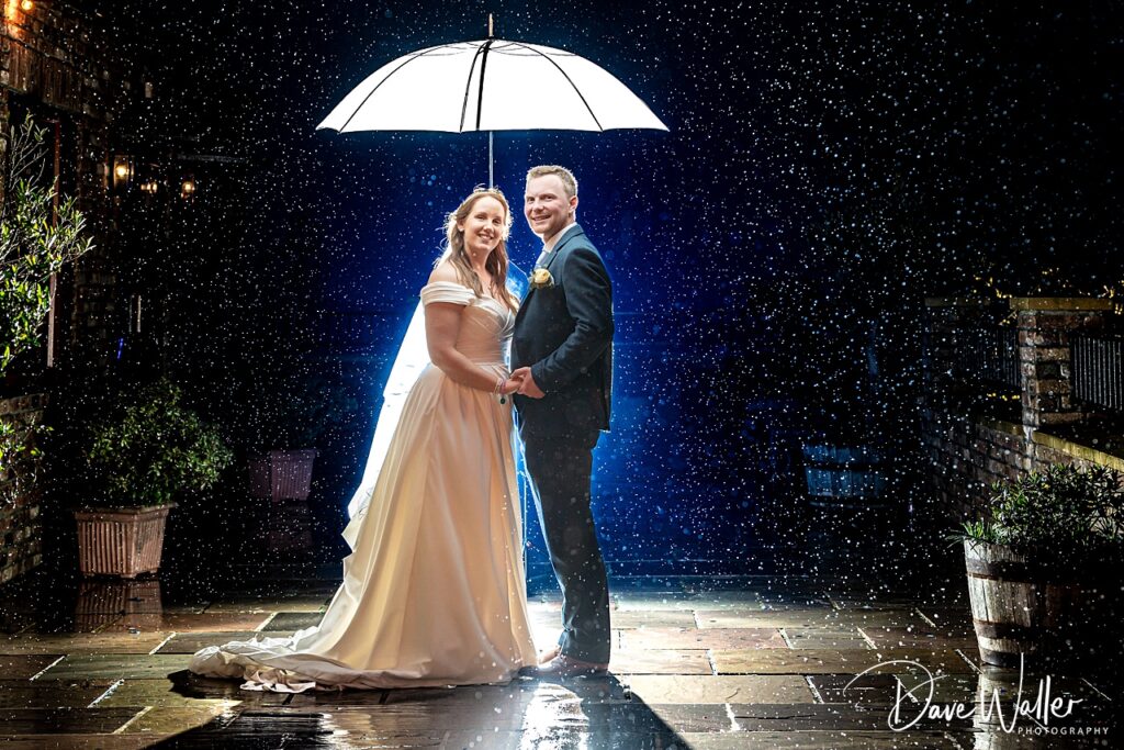 Couple under umbrella in rain, wedding photo.