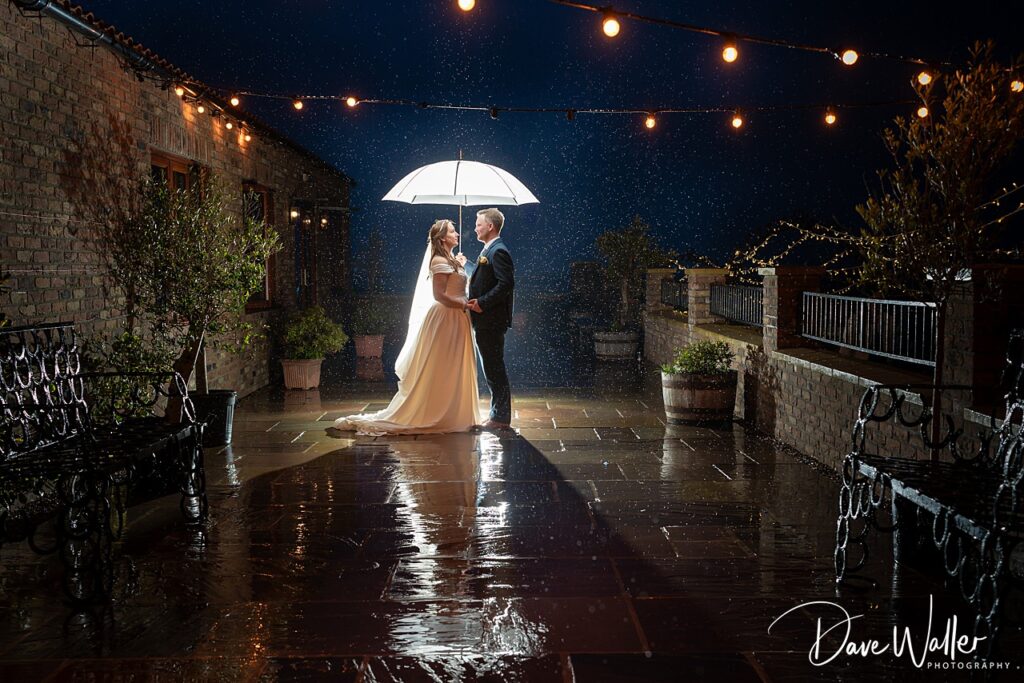 Couple under umbrella in rainy night garden wedding
