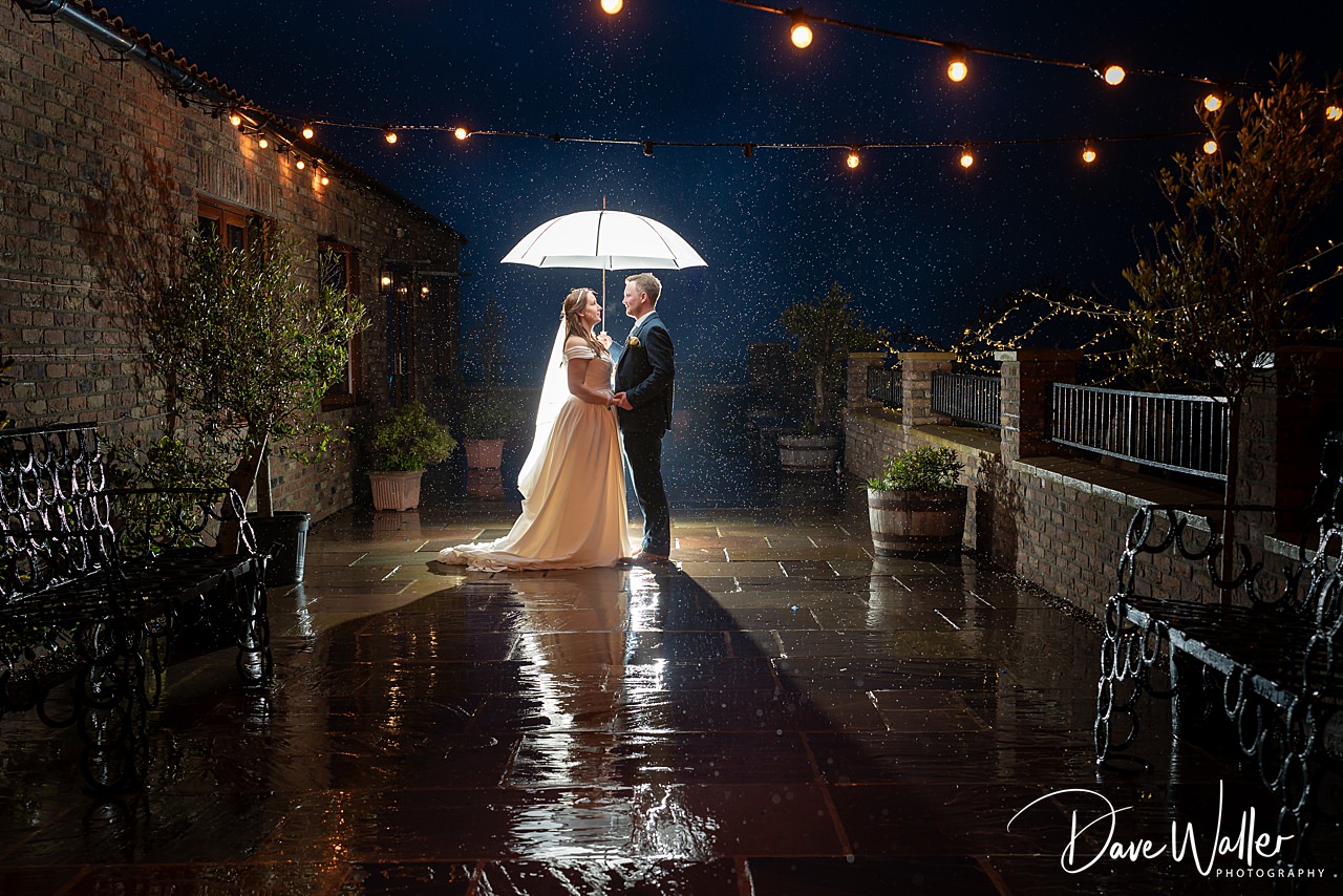 Couple under umbrella in rainy night garden wedding