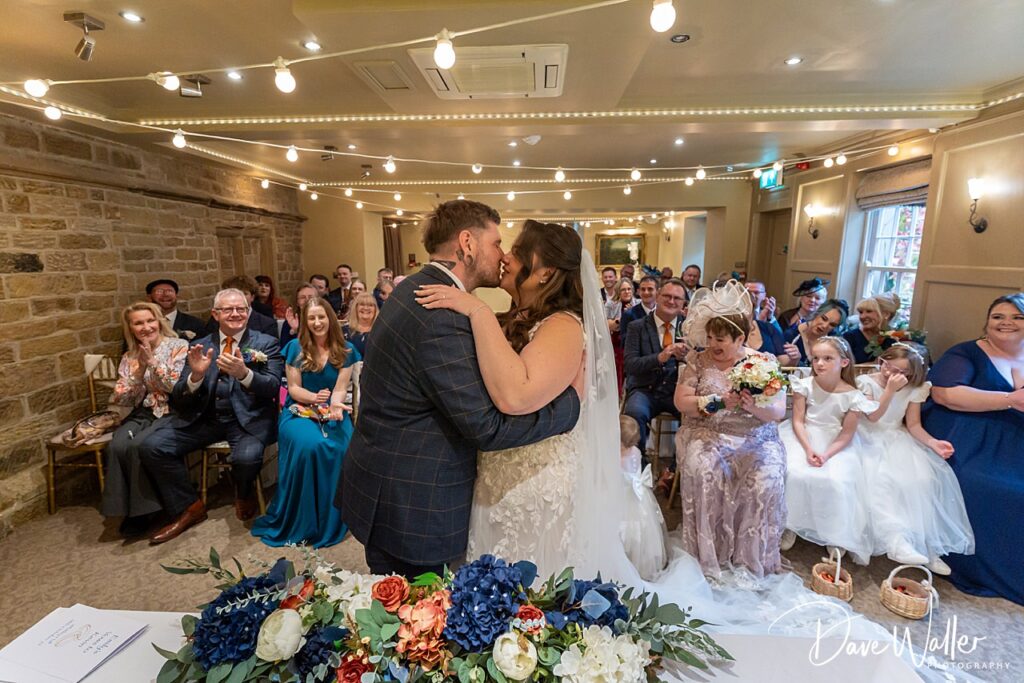 Bride and groom kiss at indoor wedding ceremony.