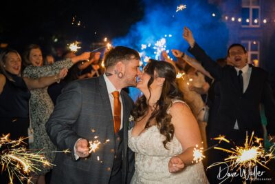 Wedding couple kissing with sparklers and guests celebrating