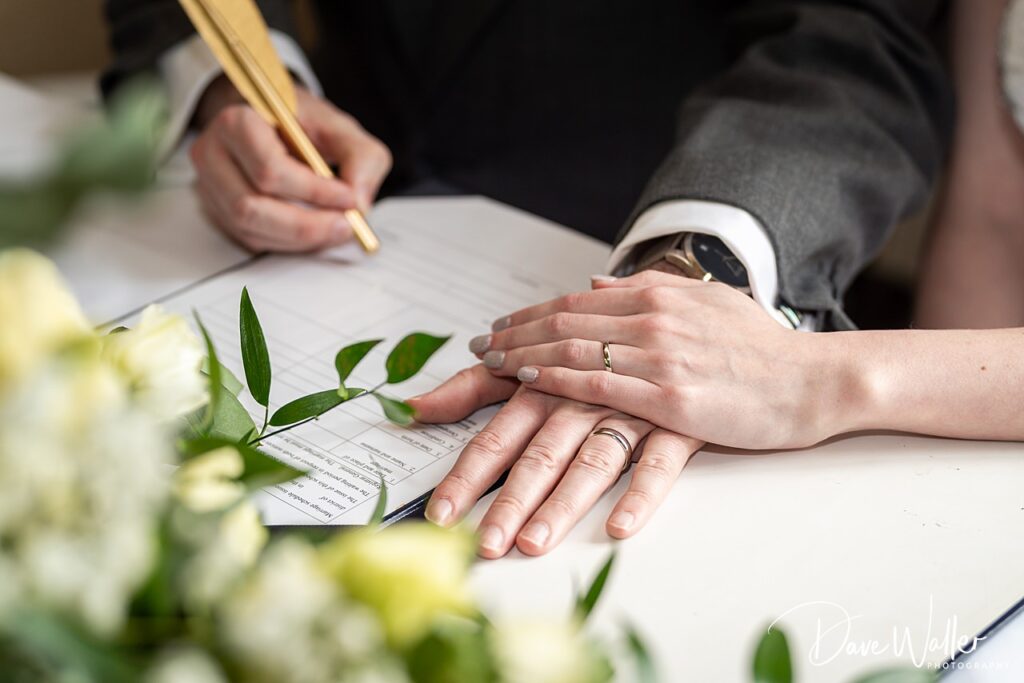 Hands with wedding rings signing marriage certificate.