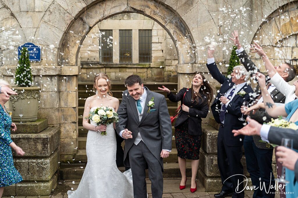 Couple walking under arch, guests throwing confetti.