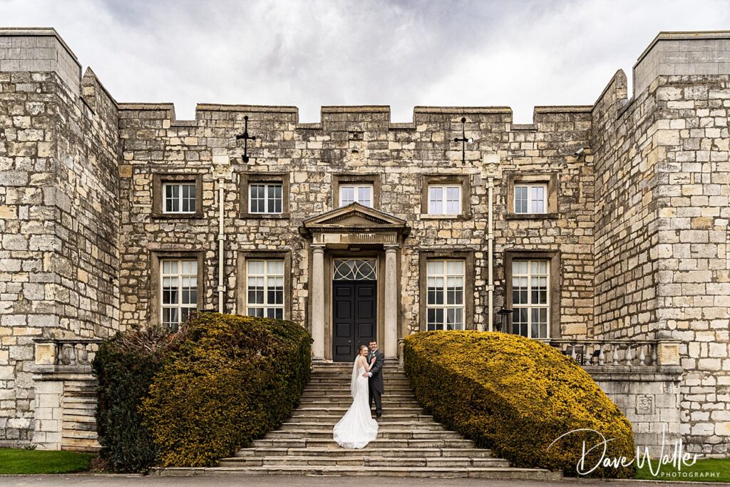 Newlyweds on steps of historic stone building.