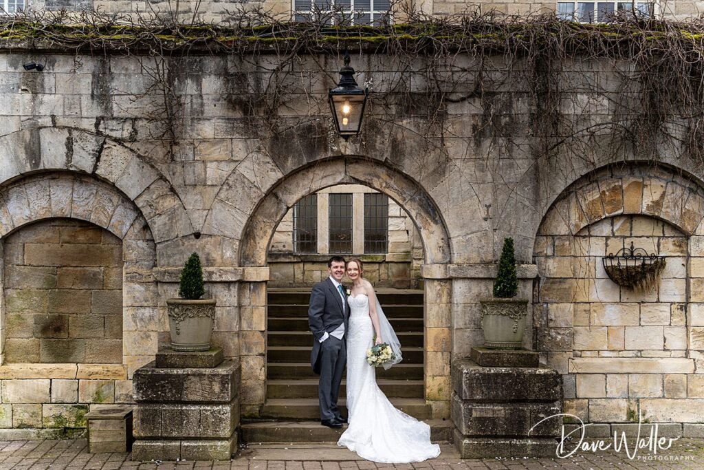 Smiling couple under stone archway at wedding.