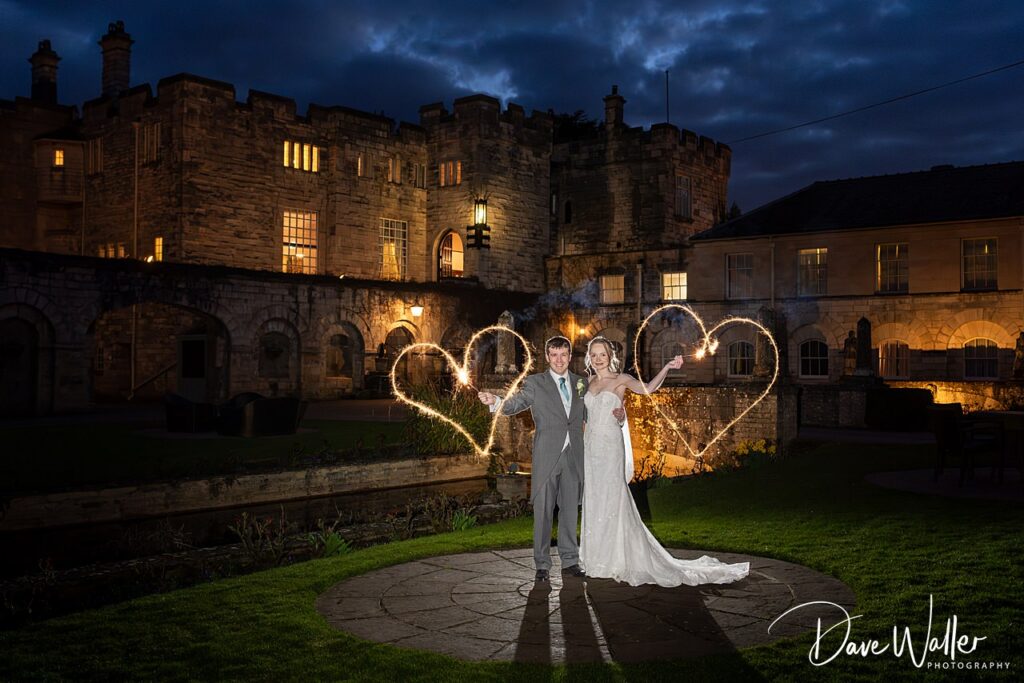 Wedding couple with sparklers outside castle at night.