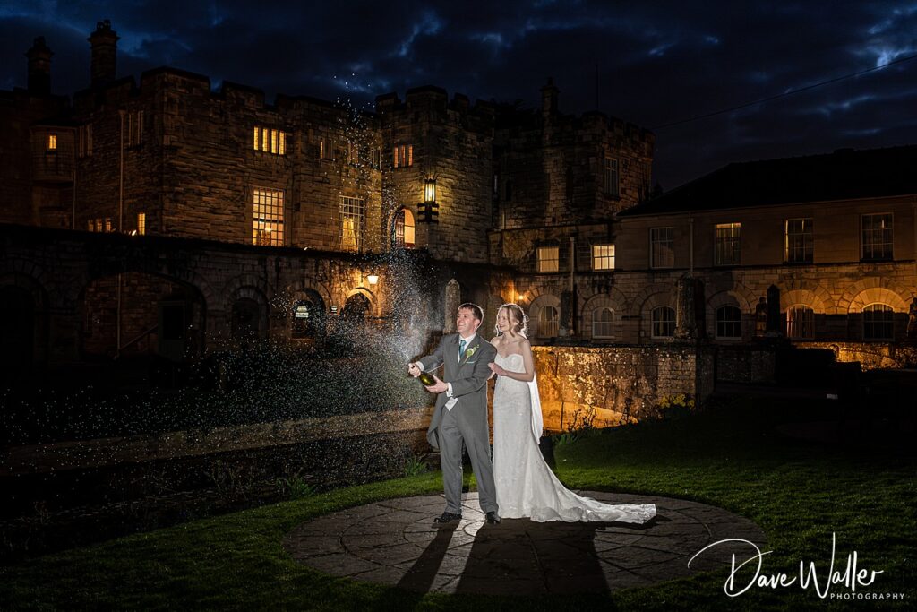 Couple celebrates at night with champagne outside castle.