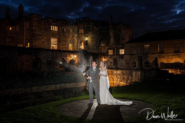 Couple celebrating with champagne outside illuminated castle.