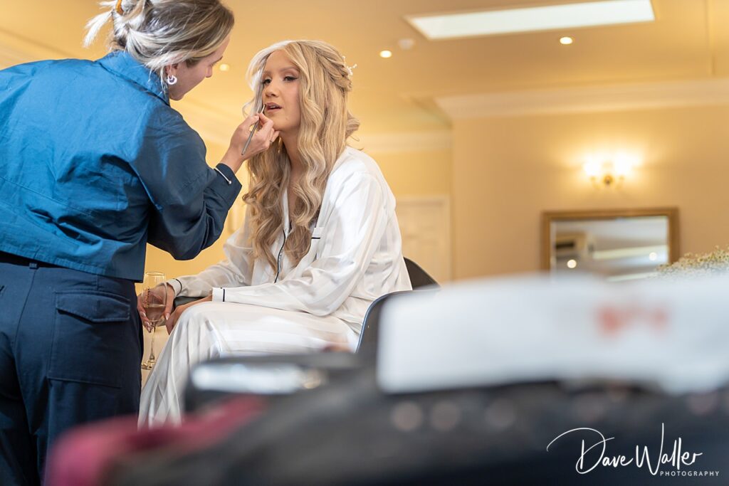 Makeup artist preparing bride with champagne glass