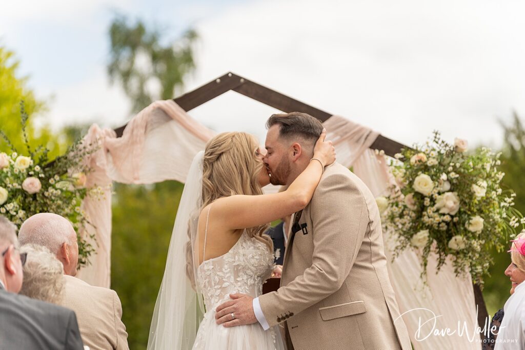 Bride and groom kiss at outdoor wedding ceremony.
