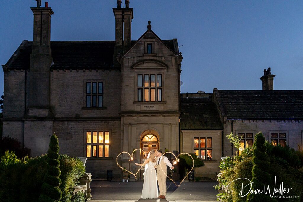 Couple with sparklers outside elegant mansion at night.