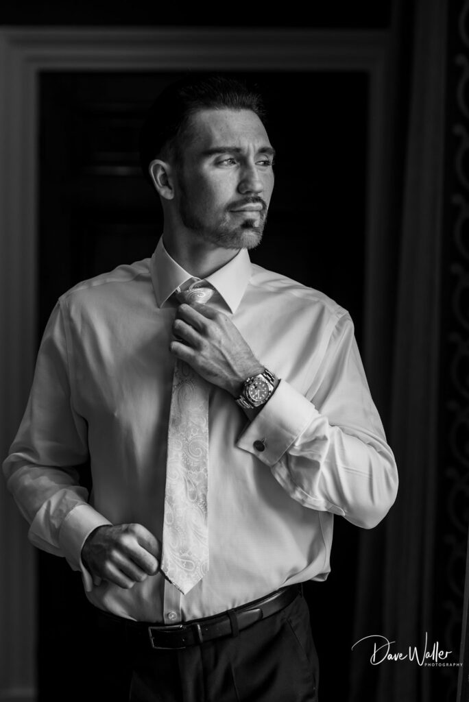 Man in formal attire adjusting tie, black and white.