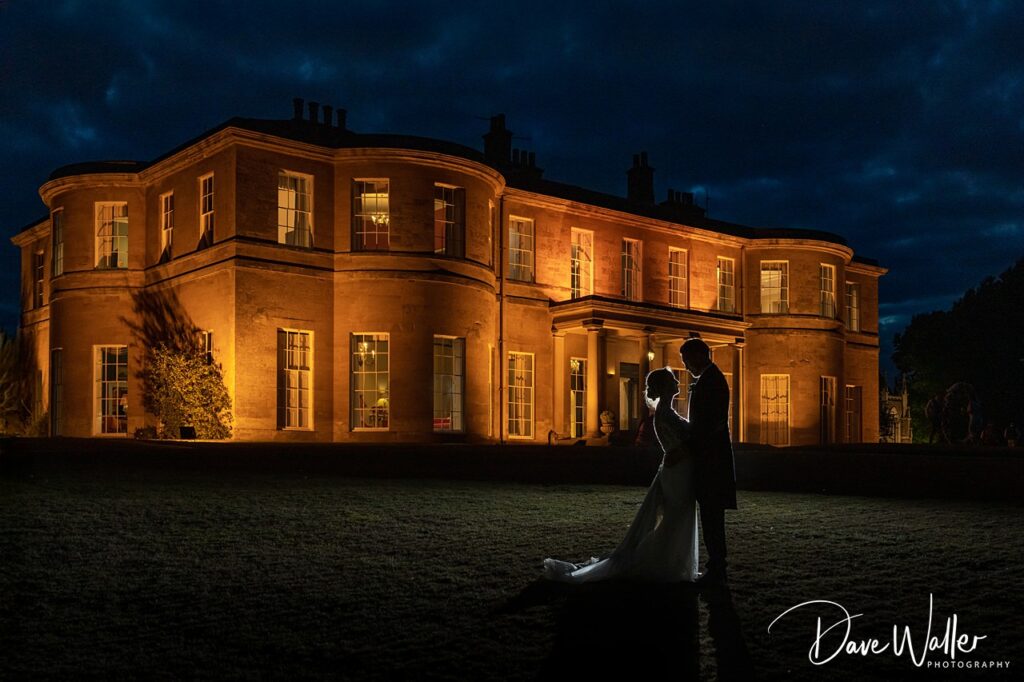 Couple silhouetted at night against lit manor house.