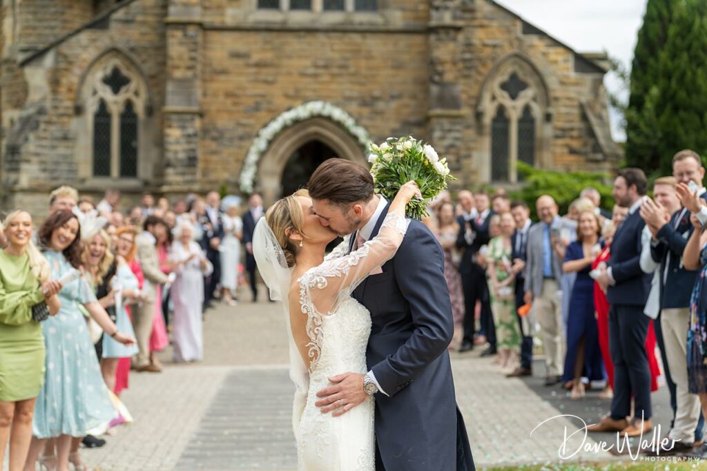 Newlyweds kiss outside church, guests clap.
