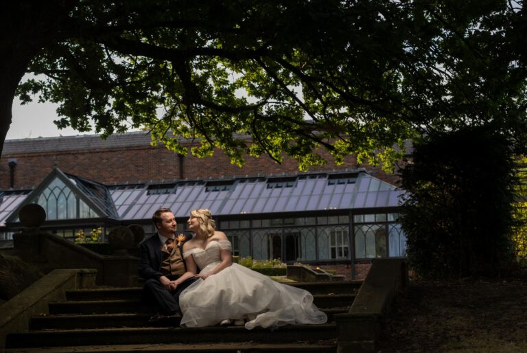 Kinga and Sean sitting on the garden steps beneath a tree by the glass house