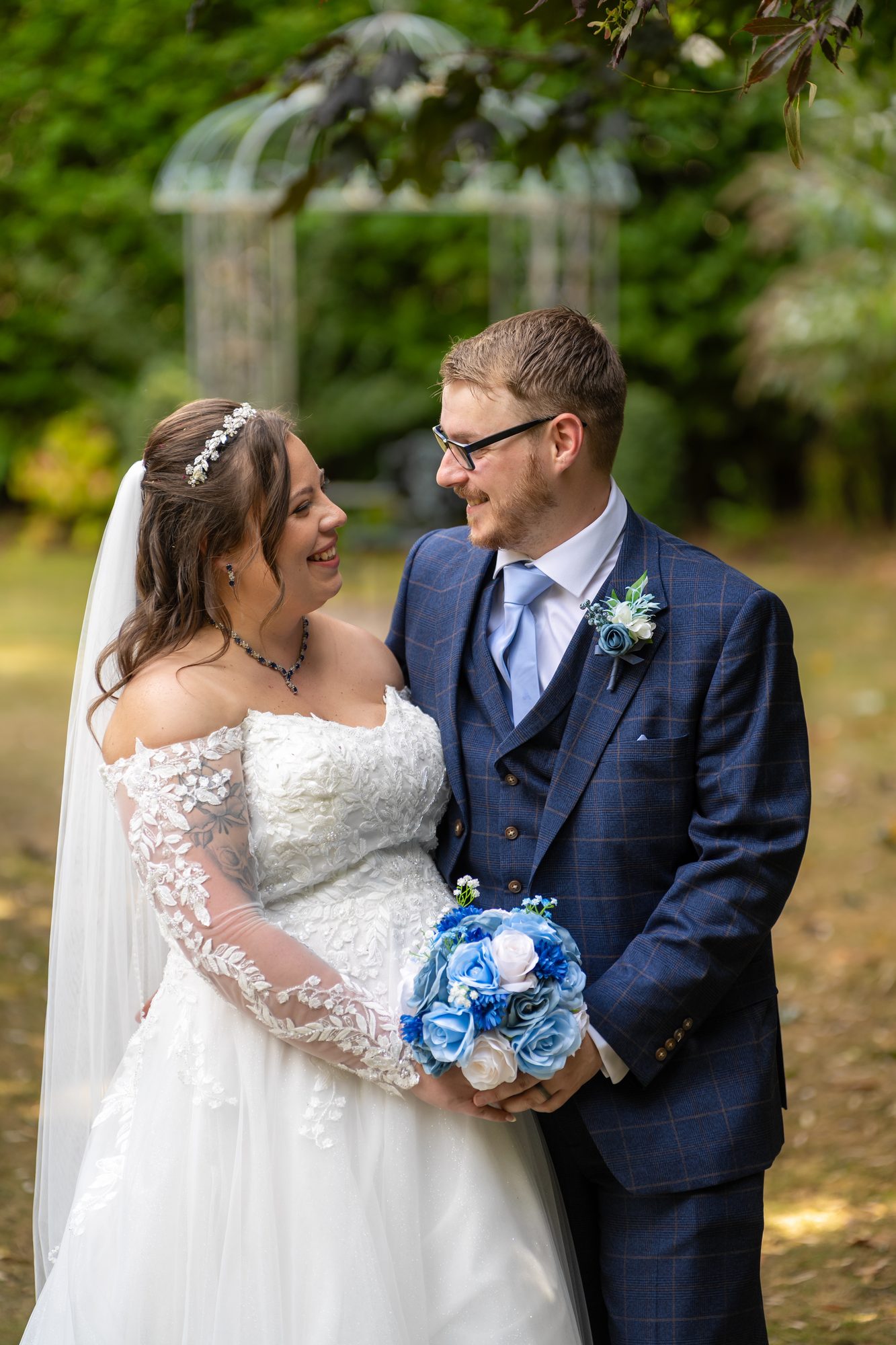 Shannon and Scott laughing together with her blue bouquet by the garden gazebo