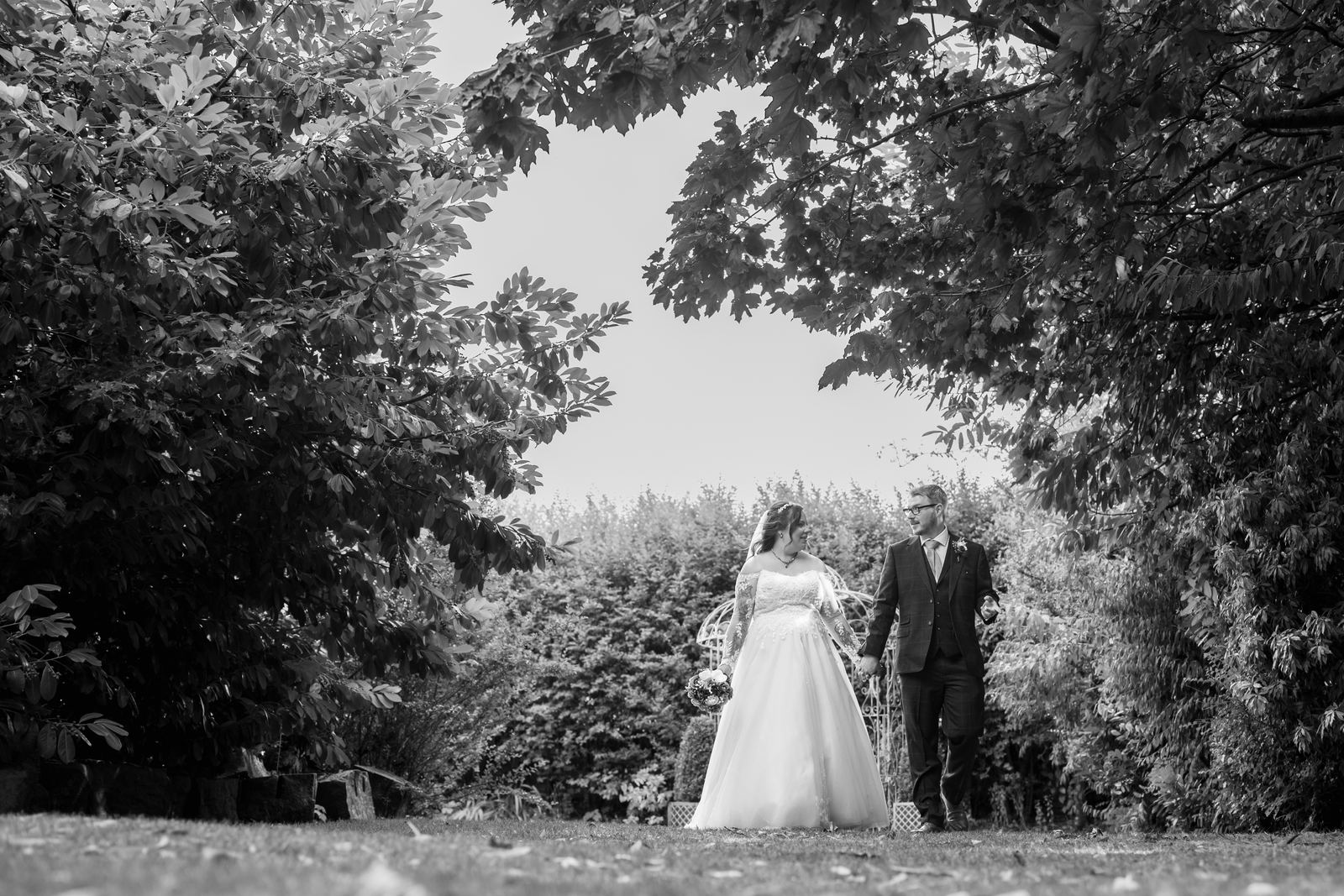 Black and white portrait of the couple among the tall trees at Holdsworth House