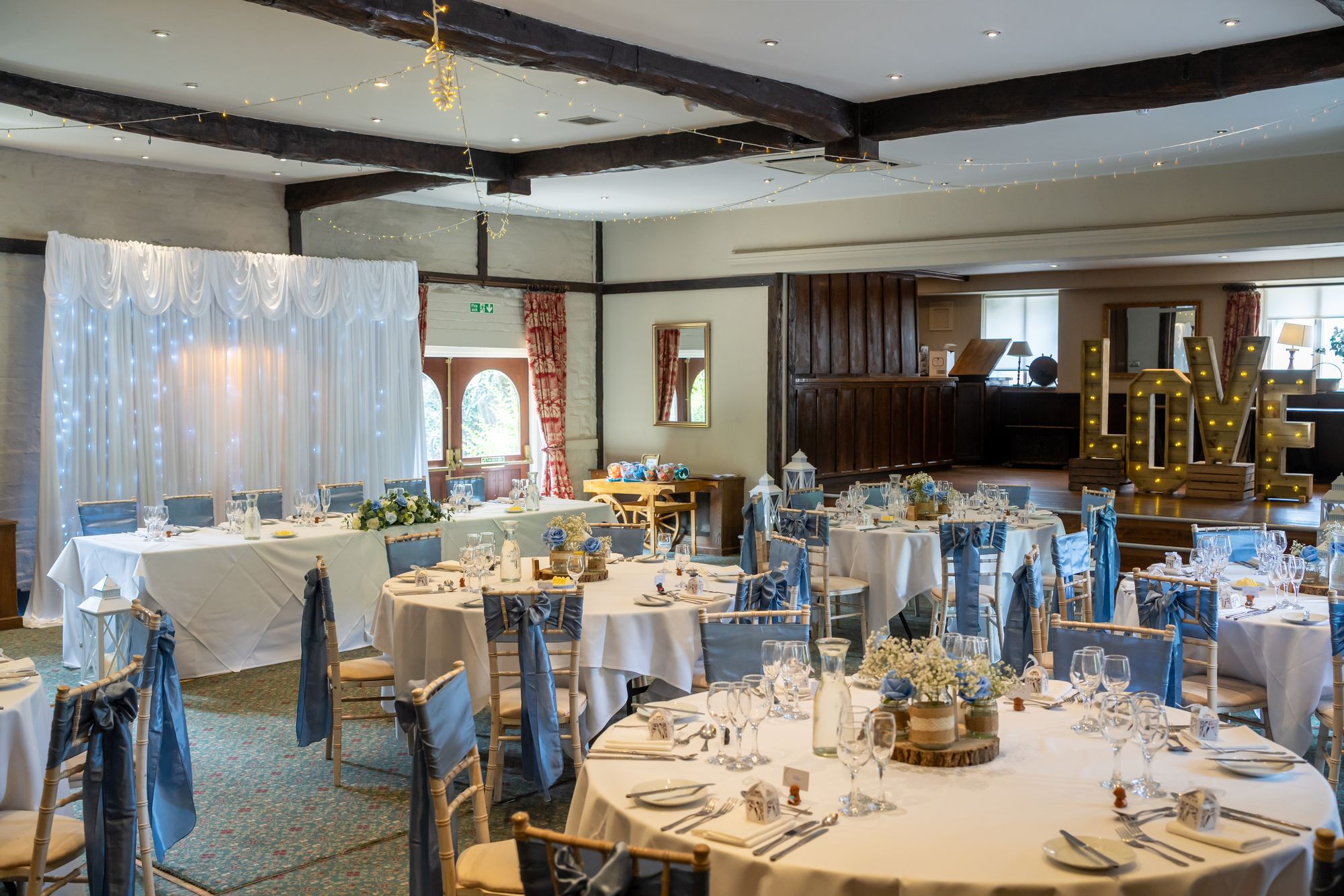 Round tables dressed in blue and white with gold-rimmed plates ready for the wedding breakfast