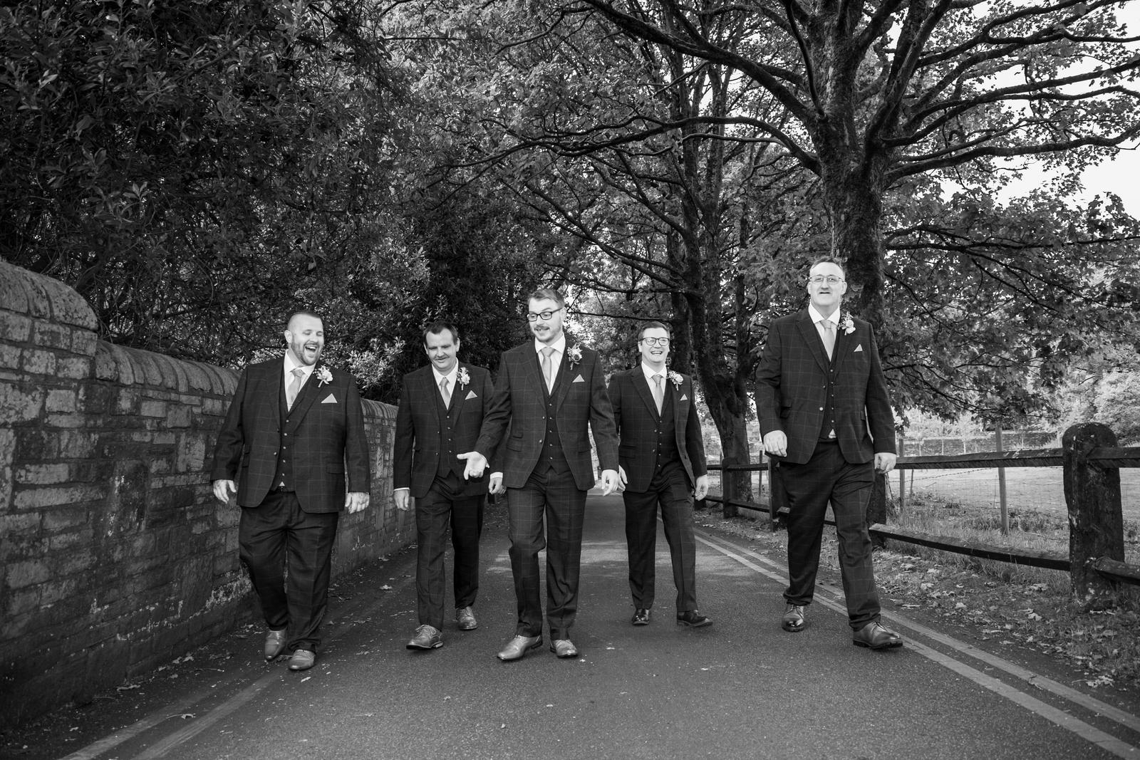 Scott and his groomsmen walking along the lane beside the old stone wall